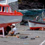 Portugal, Azores. 2006. A man does painting work at two whaling boats on a slip-way in Calheta de Nesquim village on Pico Island. Whaling was abandoned in 1986.