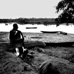 Guinea-Bissau, São Domingos, 2005. A fisherman roasts his catch on a fire near the shore of the Cacheu river at sunset.