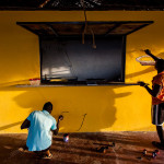 Guinea-Bissau, Cacheu. 2013. Men decorate a wall in a local bar.