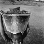 Guinea-Bissau, K3 village, at the outer marshes of the Cacheu river. 2005. A boy carries a bucket with silt from the river forelands that were once fertile rice fields. The cultivation of rice, the most important staple in the country, became impossible due to the salting up of the fields. At home, they filter and boil the silt with water and obtain good quality salt.