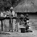 Zimbabwe, Mvurwi. 1988. Shona sculptures on display in front of the house of sculptor Samwell Chirume at the Tengenenge community. His wife Alice is washing the dishes. Some 40 sculptors work here, producing the highly acclaimed Shona works of art.