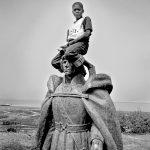 Africa, Guinea-Bissau, Cacheu. 2005. A boy sits on the same colonial statue on its new location. All colonial monuments were removed from the capital of Bissau after independence in 1974.