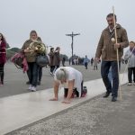 Portugal, Estremadura, Cova de Iria, Fatima. 2016. A woman is being accompanied by her family carrying large candles while she crawls on her knees as penitential exercise towards the chapel at the square of the Sanctuary of Fatima with a huge crucifix on the background. On May 13, 2017 Pope Francis will attend the celebrations of the first centenary of six apparitions of the Holy Virgin Mary to three shepherd children.