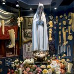 Portugal, Estremadura, Cova de Iria, Fatima. 2016. Display in the Sanctuary museum with the statue of Our Lady of Fatima surrounded by ex-votos, photographs, banners, flowers and medaillons.