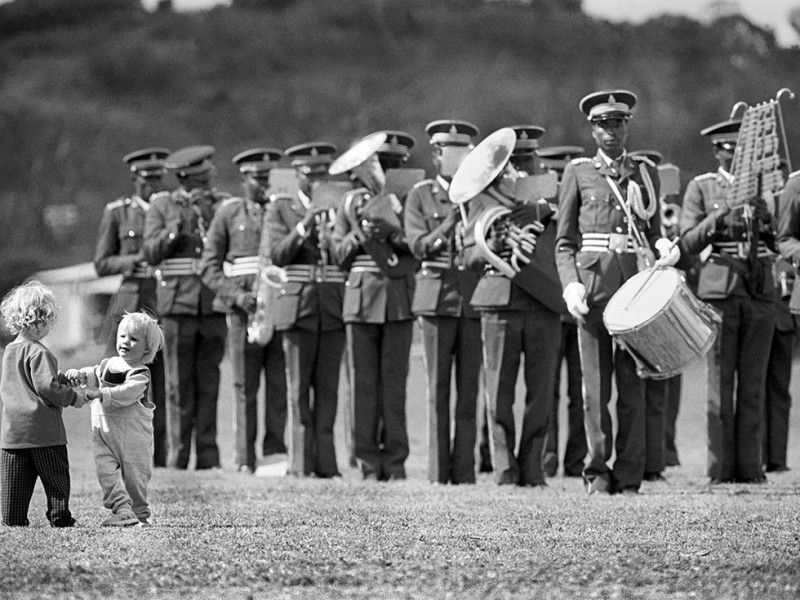 Zimbabwe, Domboshawa. 1989. A military band plays while two little children dance on the lawn.